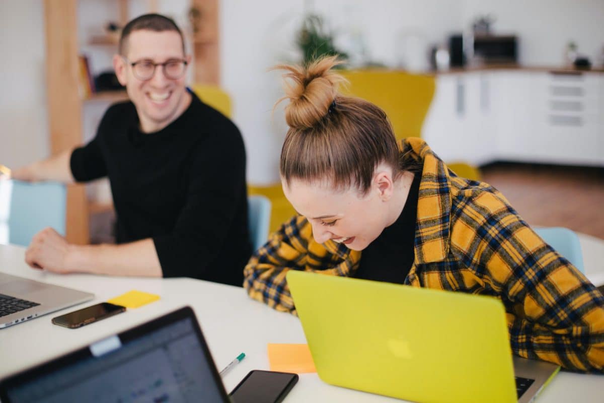 Group of people laughing while sat with laptops