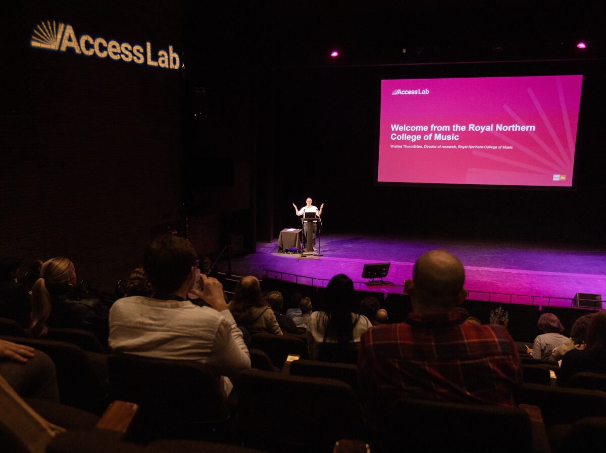 Image shows Access Lab EMEA attendees sitting down in a theatre listening to the speaker who is on the podium.