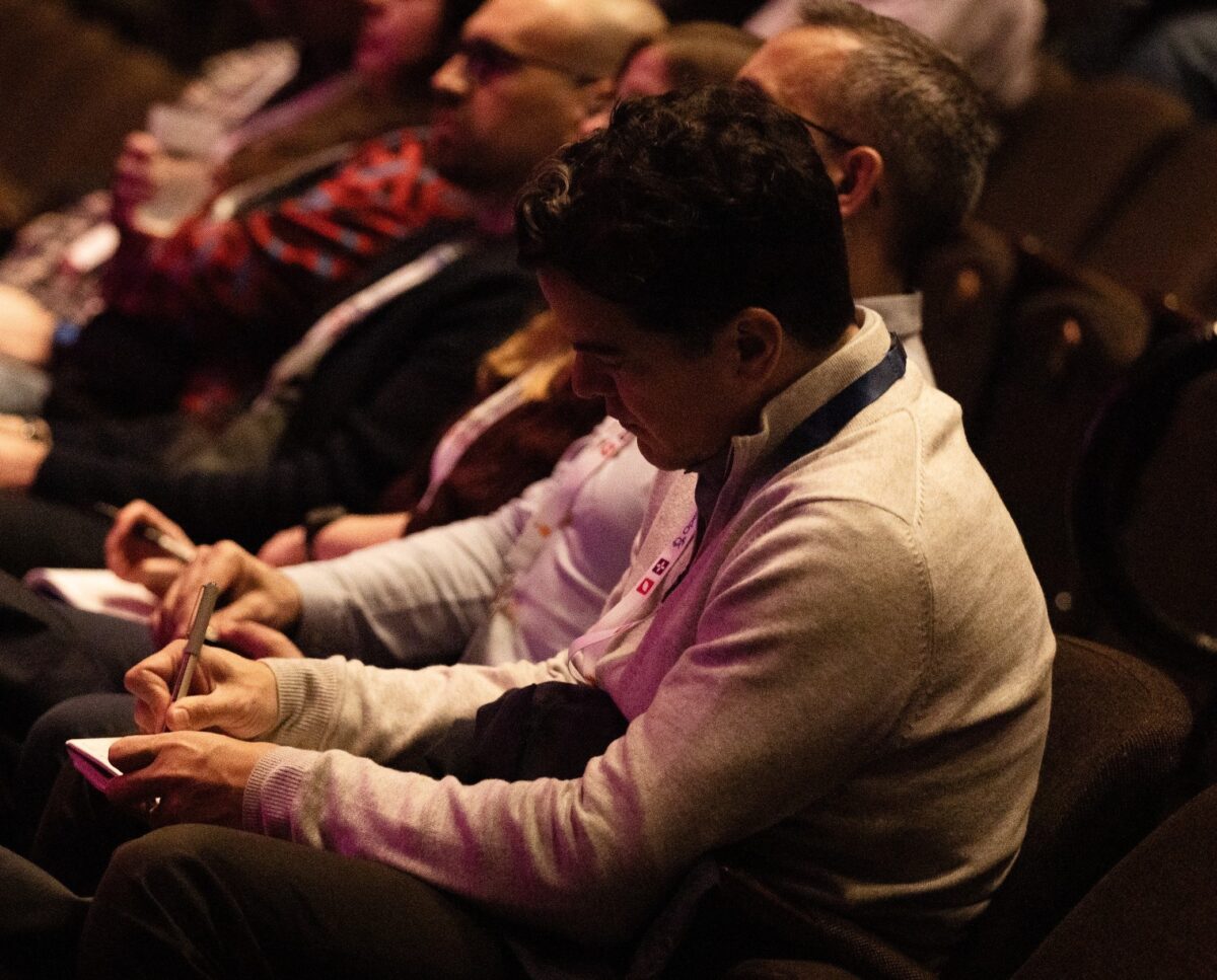 Image shows a man writing notes whilst sat down in a theatre.